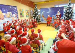 Kilka grup dzieci siedzi na krzesełkach wokół pani dyrektor Marii Królikowskiej, która czyta legendę o świętym Mikołaju.